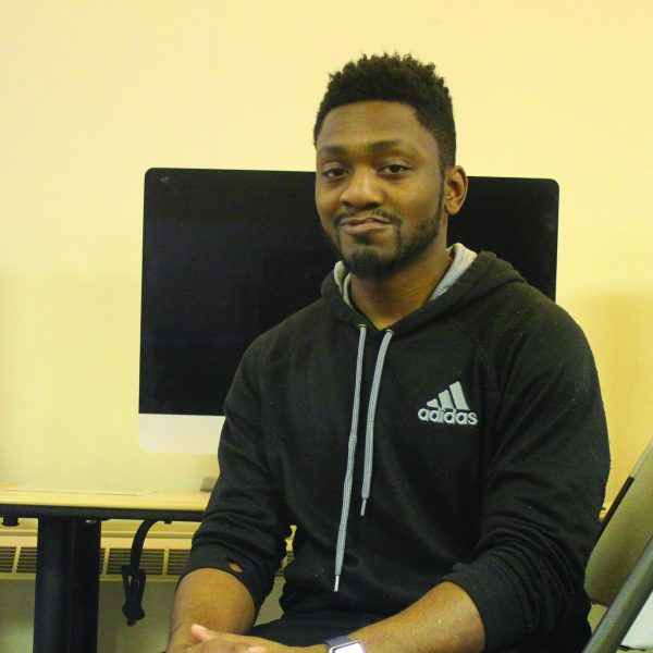 Smiling towards the camera, a young man with hopes of becoming an IT professional sits in a computer lab.