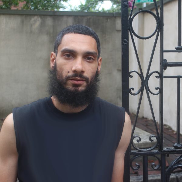 Smiling towards the camera, a young man stands outside a church to share his story.