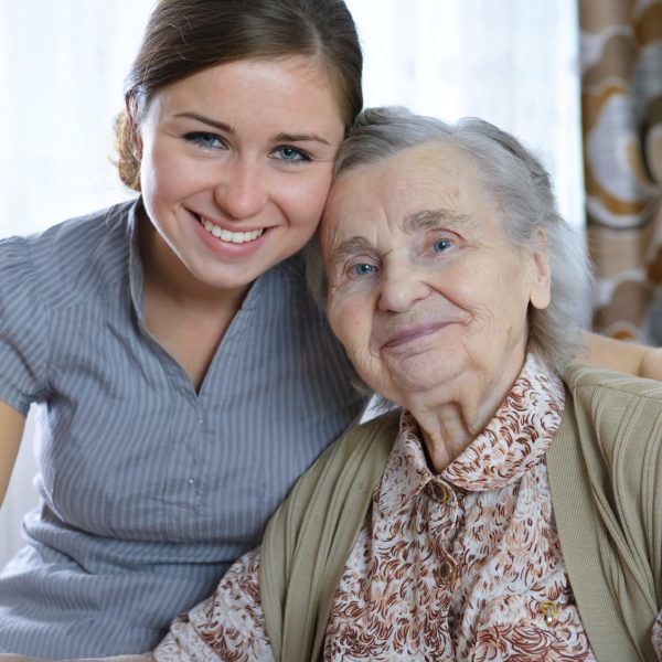 A elderly woman sits with a younger lady, perhaps her granddaughter, neighbor, or friend. Both smile to the carmera.